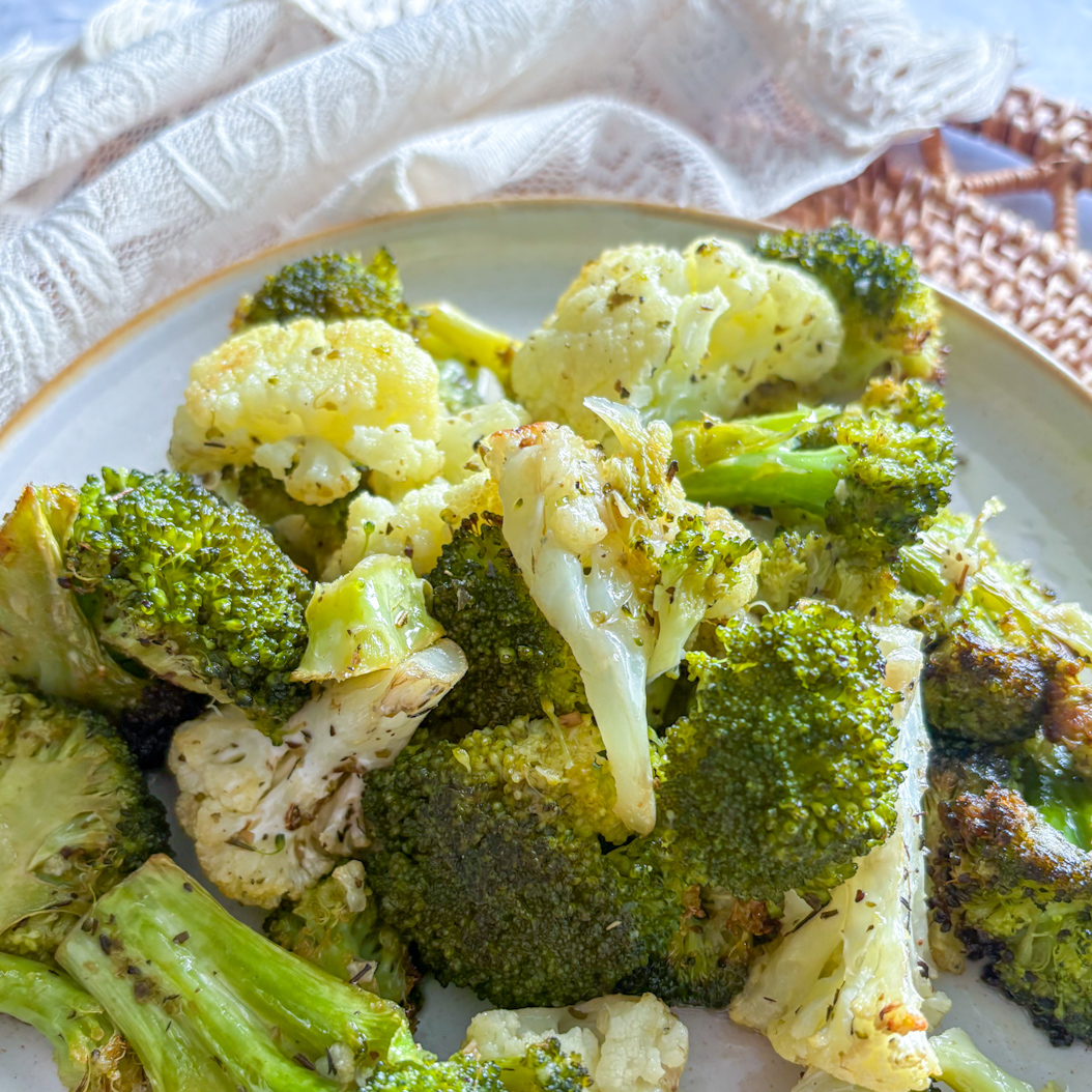 Side view of herby roasted broccoli and cauliflower served on a white ceramic plate.