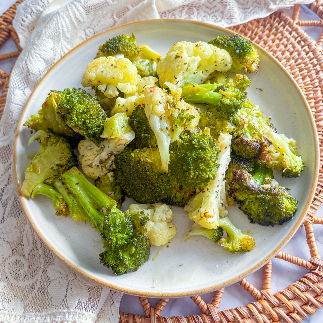 Roasted broccoli and cauliflower on a plate with crisp edges, served on a neutral background.