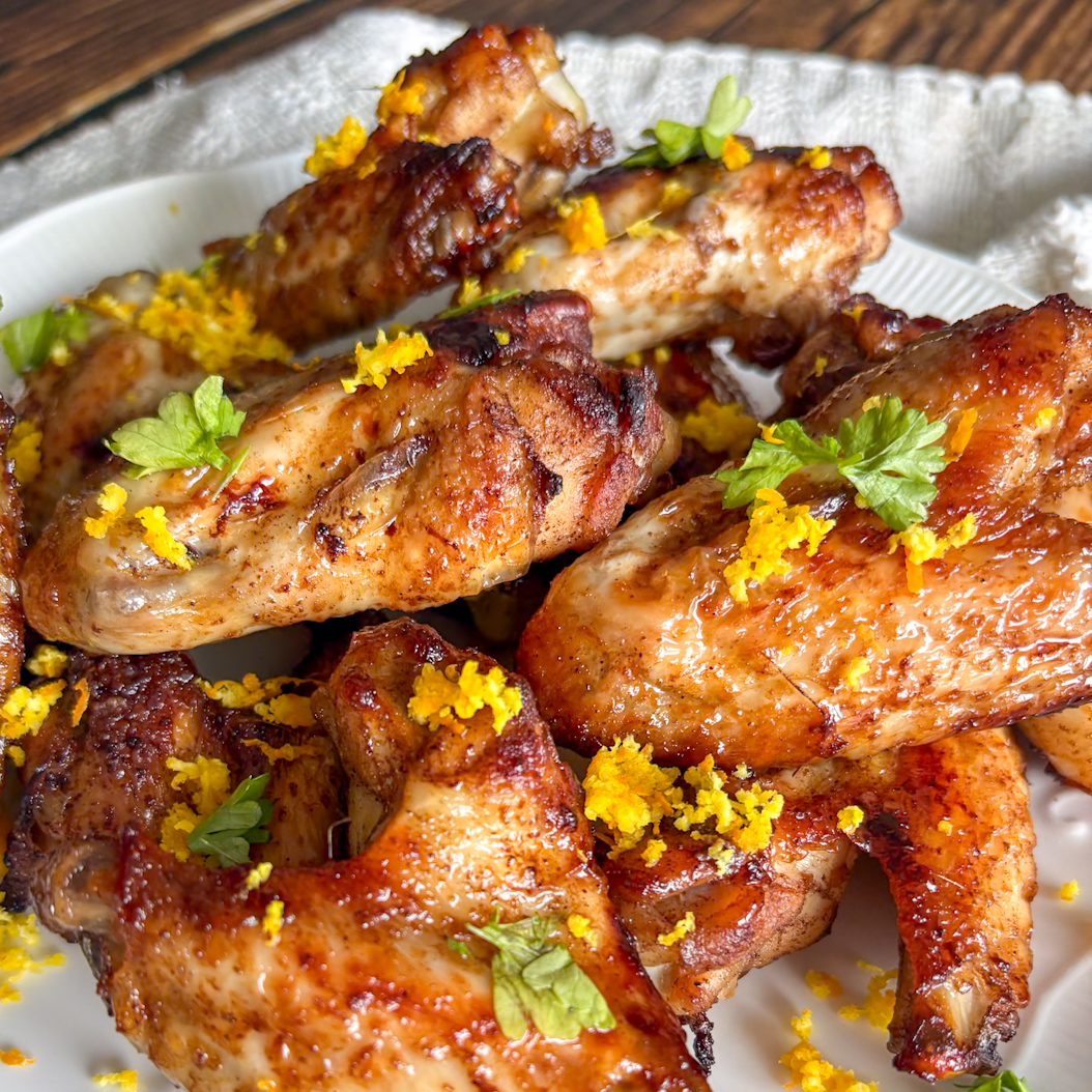 Close-up of Five Spice Chicken Wings on a white plate, garnished with orange zest and herbs.