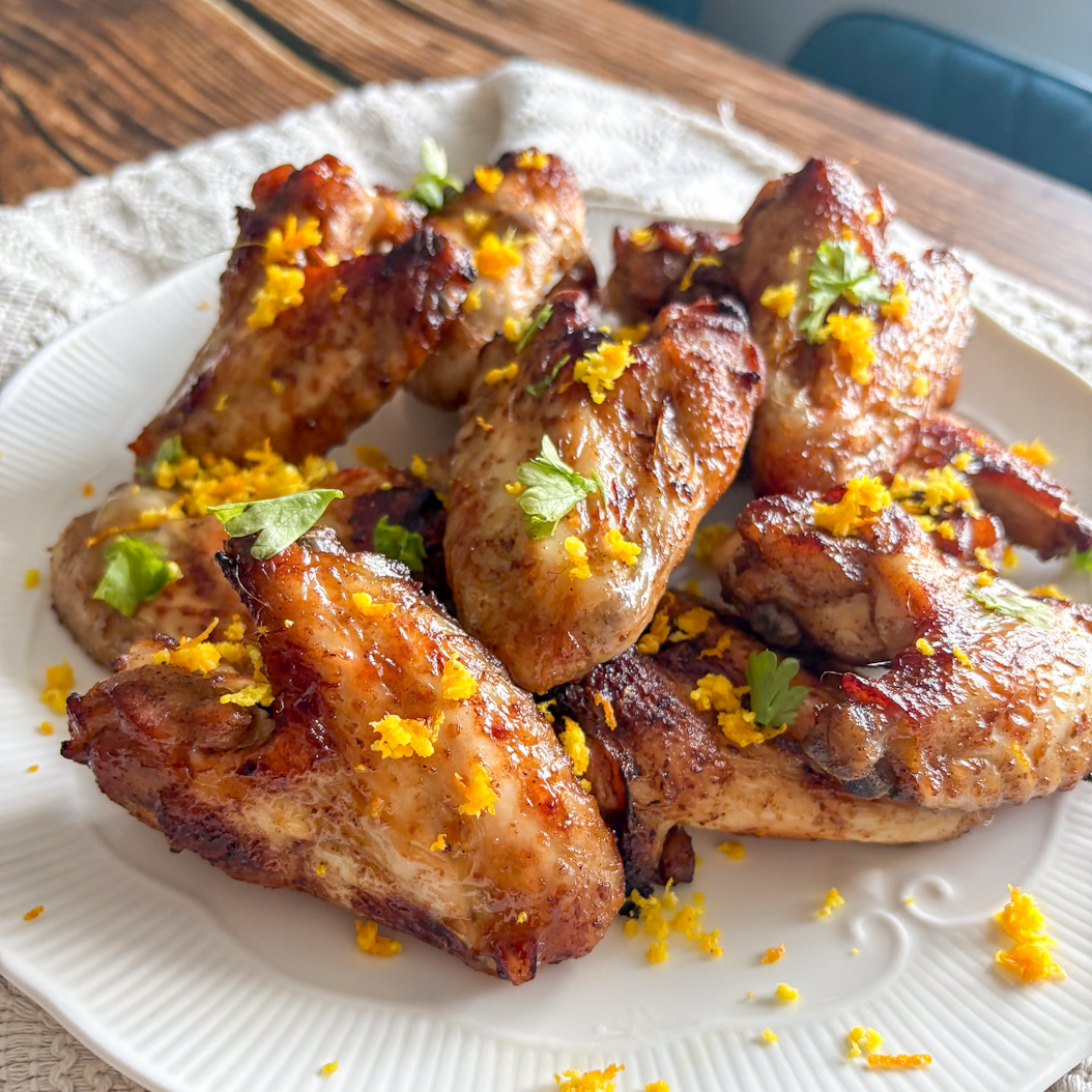 Crispy Five Spice Chicken Wings with glossy glaze, orange shreds, and parsley on a white dish.