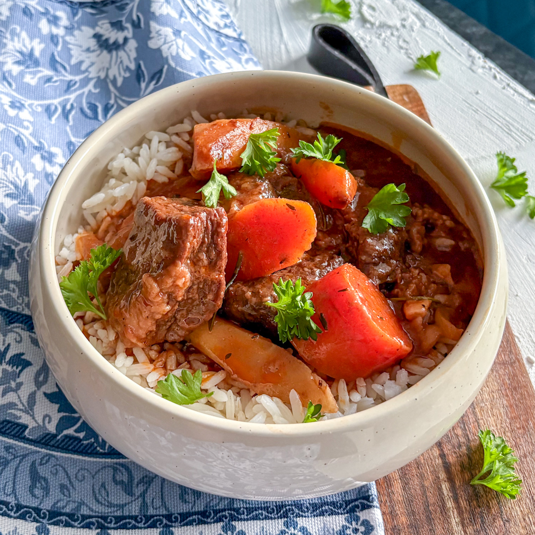 Bowl of beef stew with carrots, parsnips, and rice, garnished with parsley