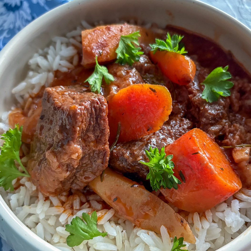 Close-up of beef stew with tender beef chunks, carrots, and rice in a ceramic bowl