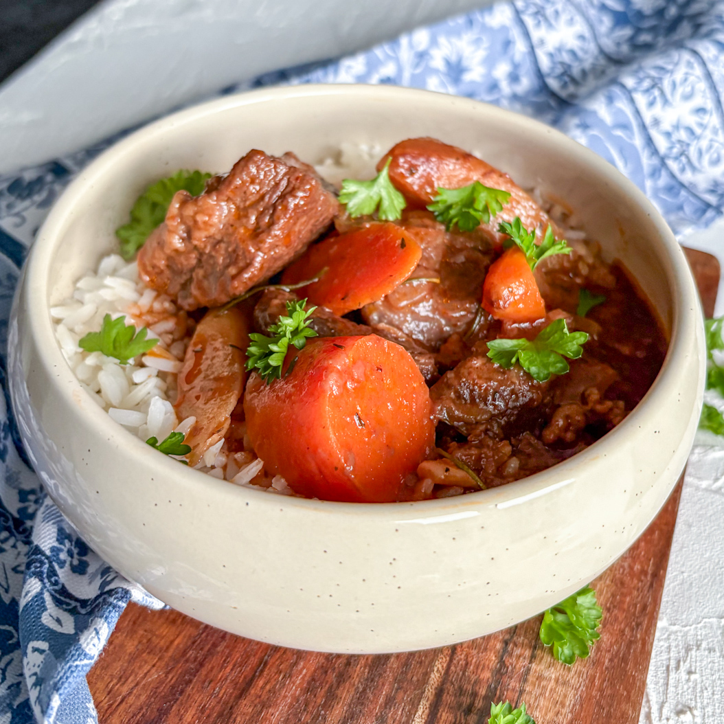 Rustic beef stew in a bowl with rice, carrots, and parsley garnish