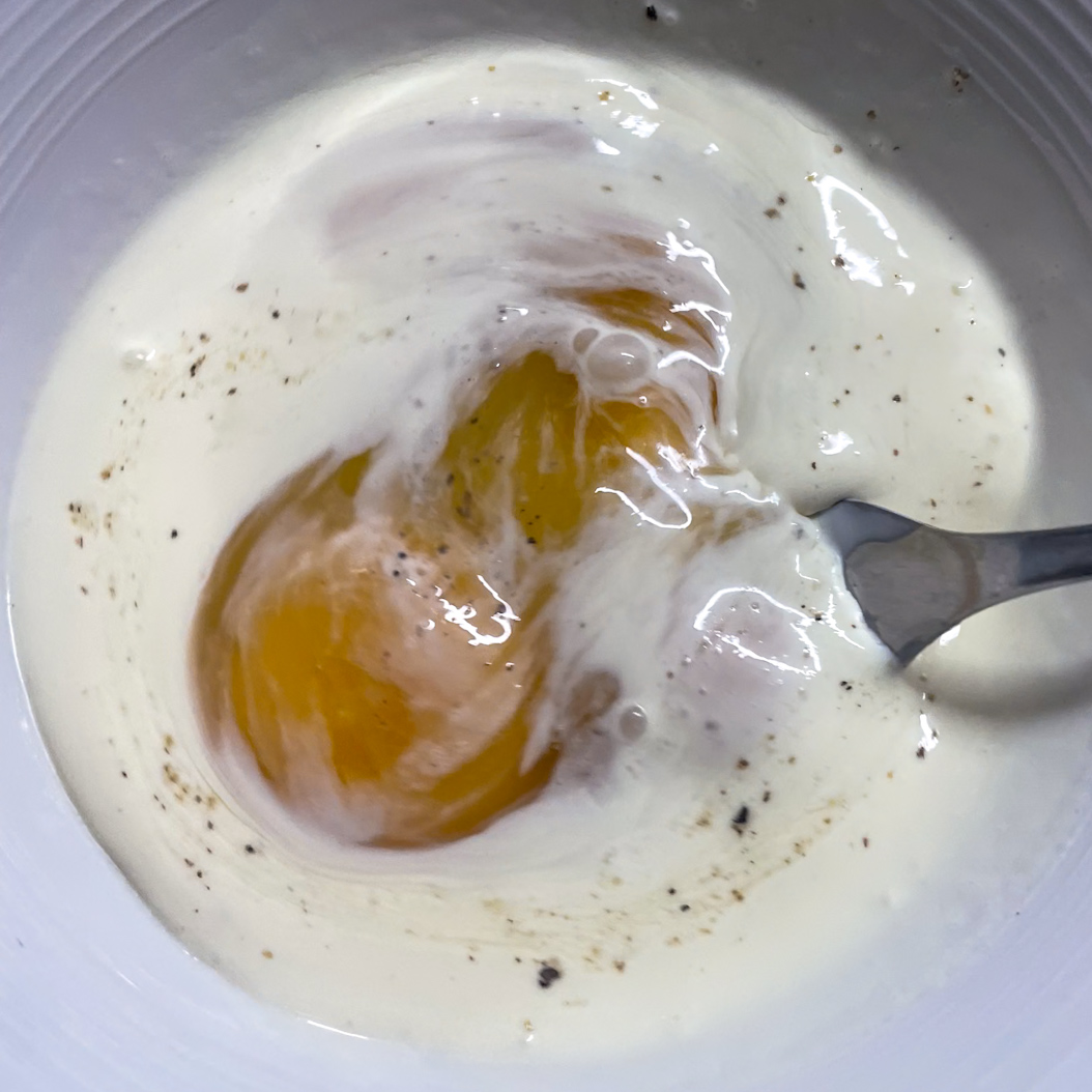 Egg yolk whisked with cream, salt, and pepper in a bowl for mushroom omelette mixture.