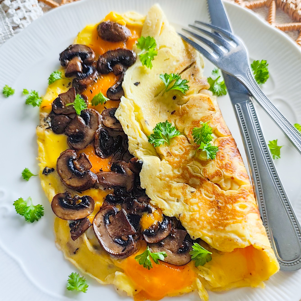 Half-folded mushroom omelette filled with cheddar and mushrooms, garnished with fresh parsley on a white plate.
