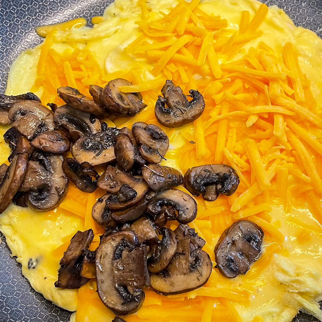 Partially cooked omelette topped with cheddar cheese and sautéed mushrooms.