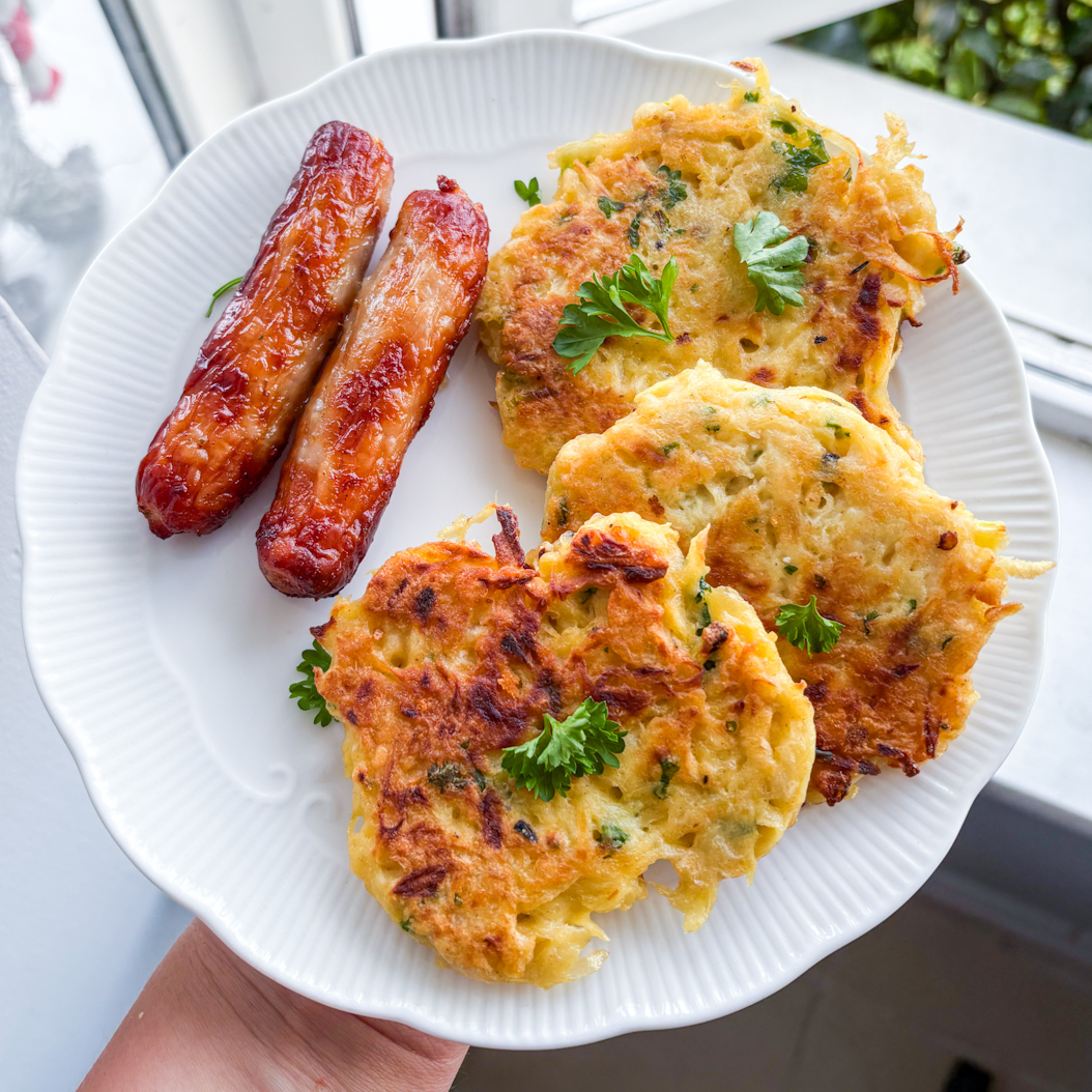 Handheld plate of golden vegetable fritters and glazed sausages, ready to eat.