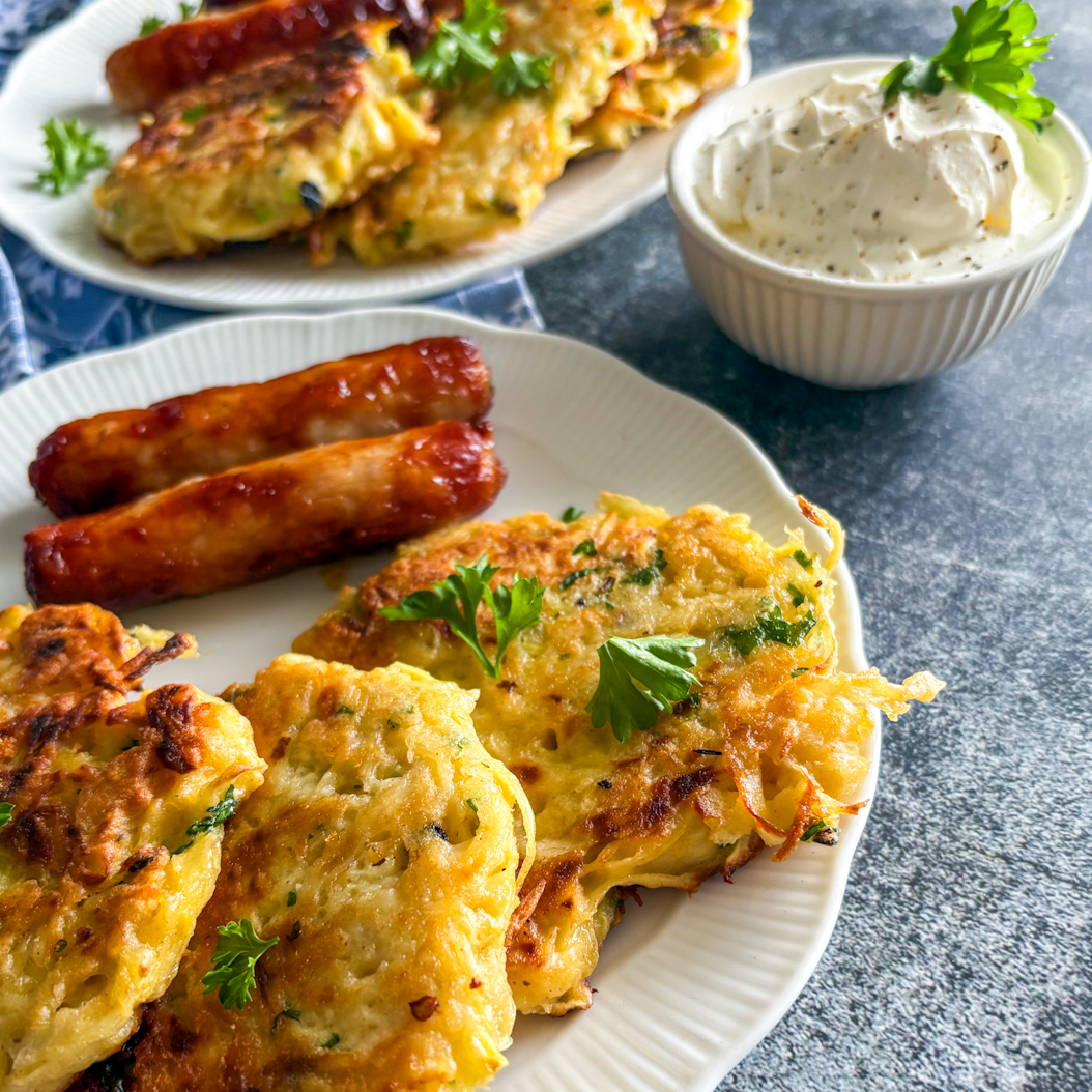 Golden vegetable fritters with sausages and creamy dip, plated for a savoury breakfast.