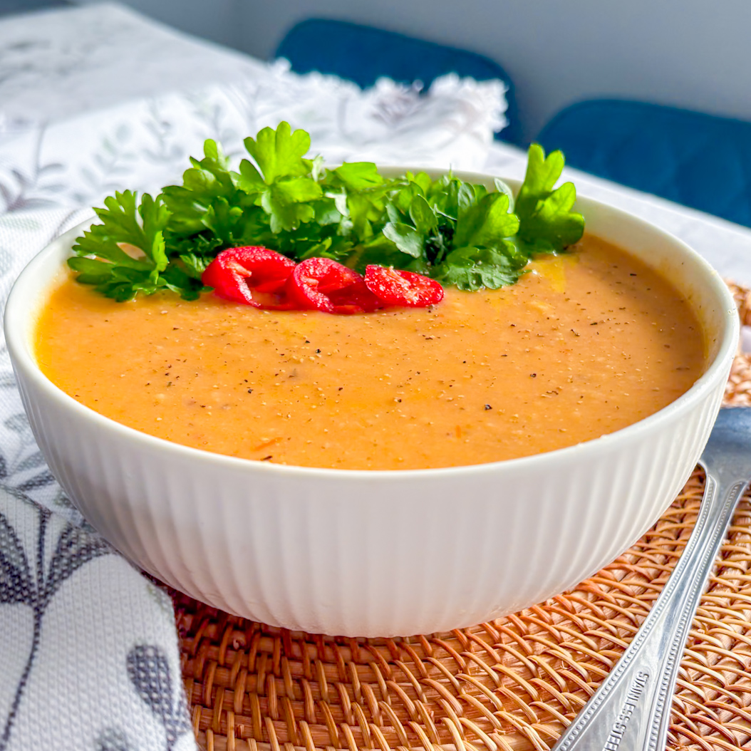 Bowl of spicy roasted parsnip soup topped with fresh parsley and sliced red chilli on a woven placemat.