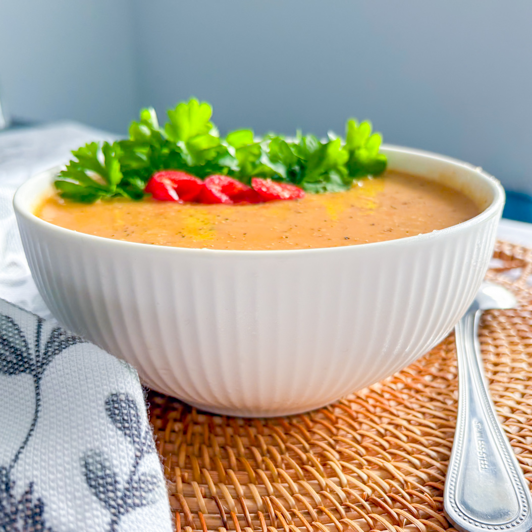 Roasted parsnip soup with chilli slices and fresh parsley, placed on a rustic placemat with a silver spoon.