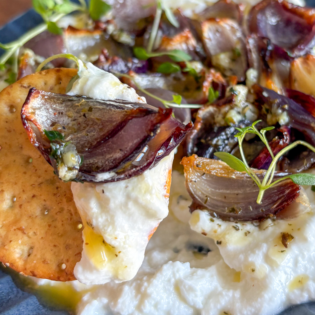 Crispy roasted red onion on cracker with ricotta and garlic butter, ready to eat.