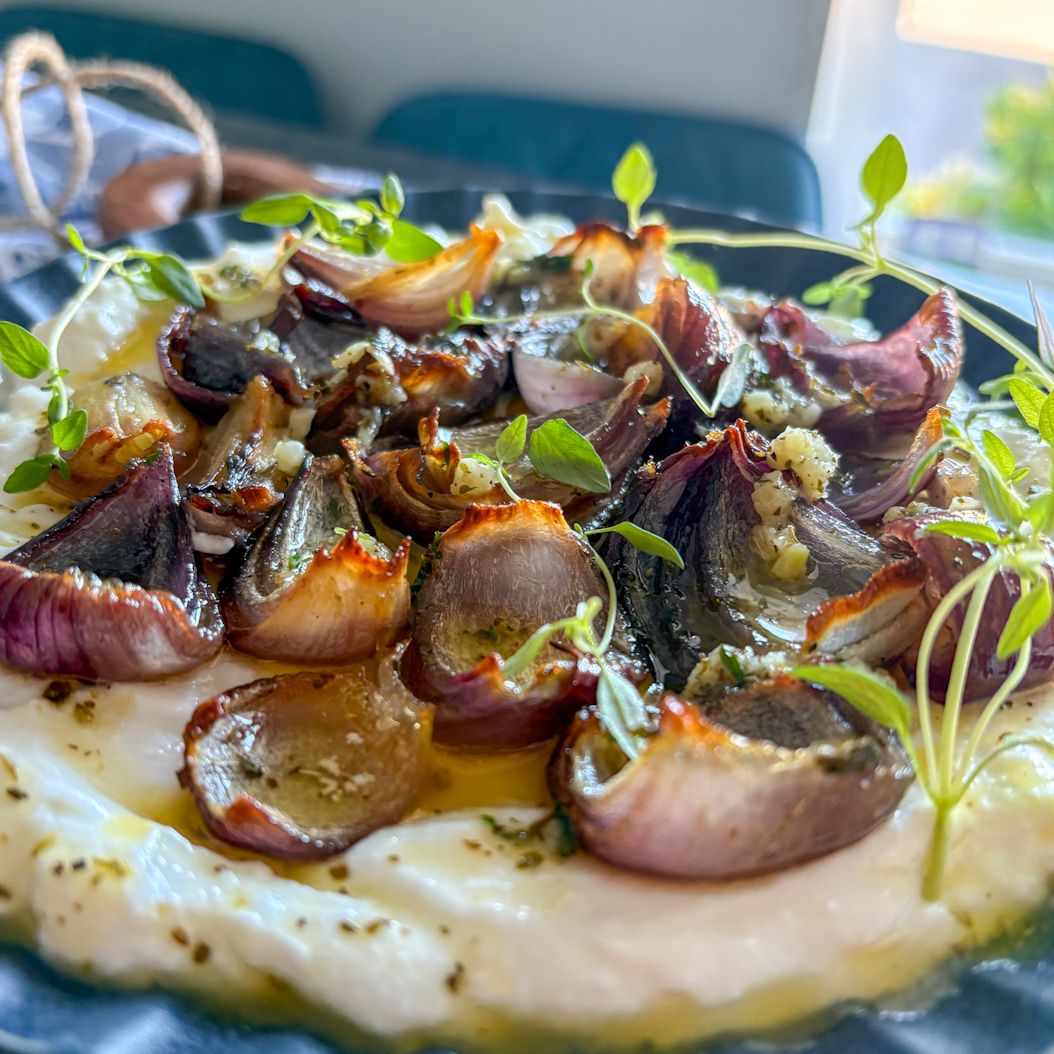 Whole serving of roasted red onions and ricotta on a round plate with fresh herbs.