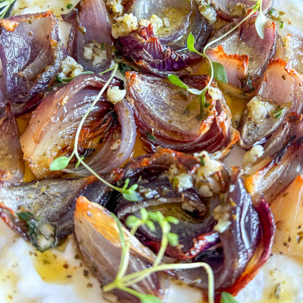 Close-up of roasted red onions on whipped ricotta, topped with garlic herb butter and fresh thyme.