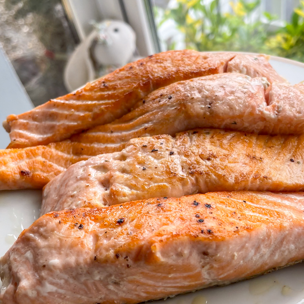 Pan-seared salmon fillets resting on a white plate, ready to be flaked for the Salmon Spinach Salad.