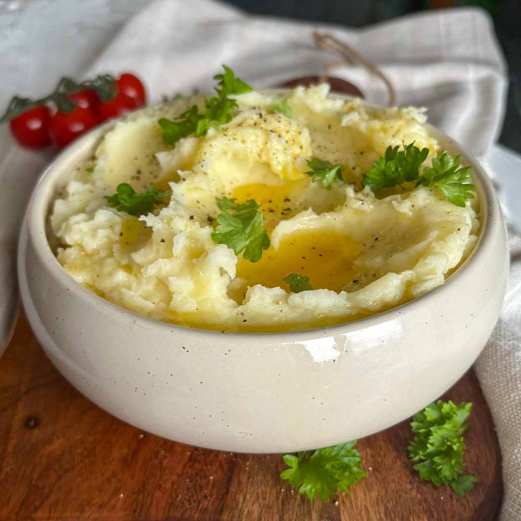 Roasted Garlic Mashed Potatoes with melted butter, parsley and black pepper in a ceramic bowl