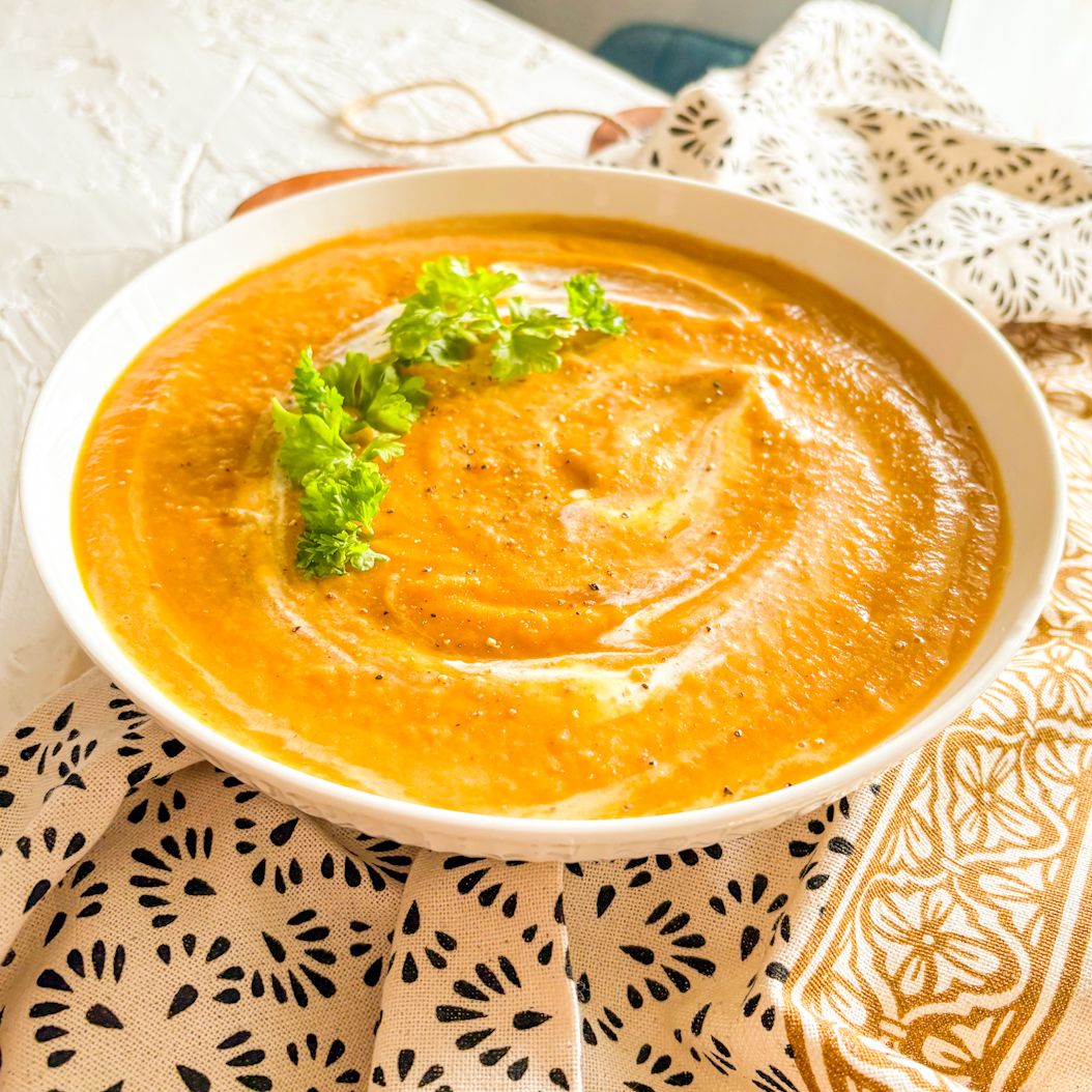 Velvety spiced carrot soup served in white bowl with cream drizzle