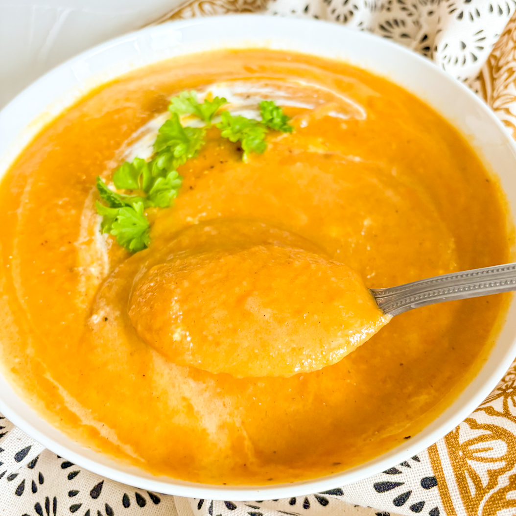 Bowl of spiced carrot soup with buttery cream swirl and fresh herbs