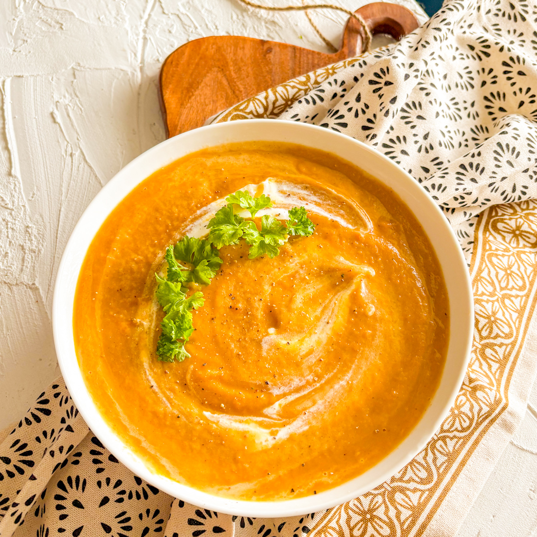 Creamy spiced carrot soup with parsley and cream swirl in white bowl
