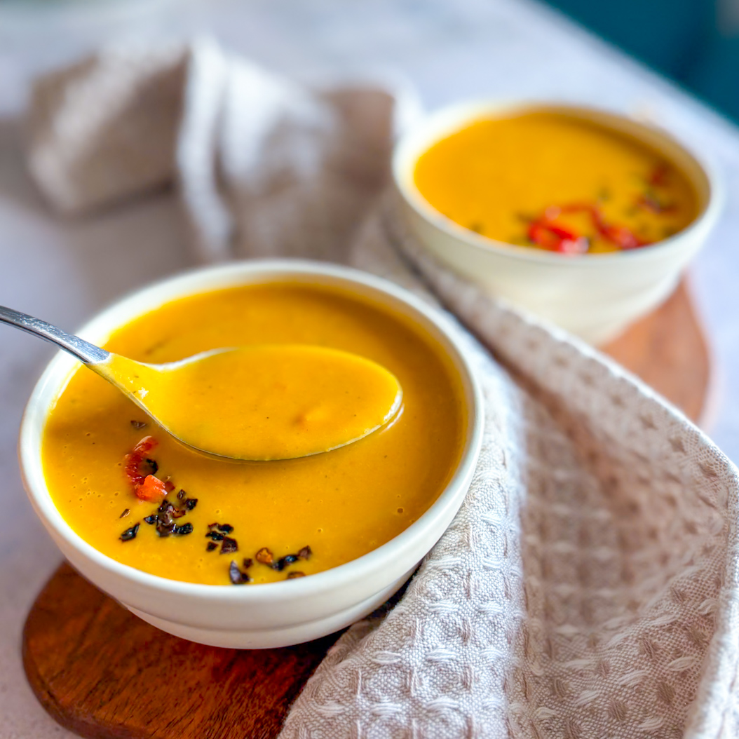 Spoon lifting creamy Sweet Potato and Carrot Soup showing smooth, silky consistency