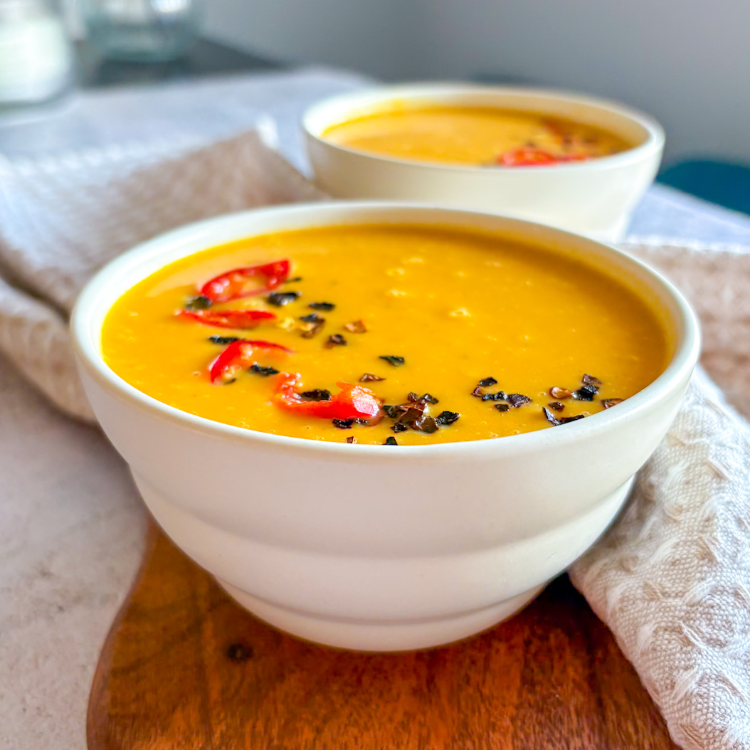 Creamy Sweet Potato and Carrot Soup served in bowls with chilli garnish on wooden board