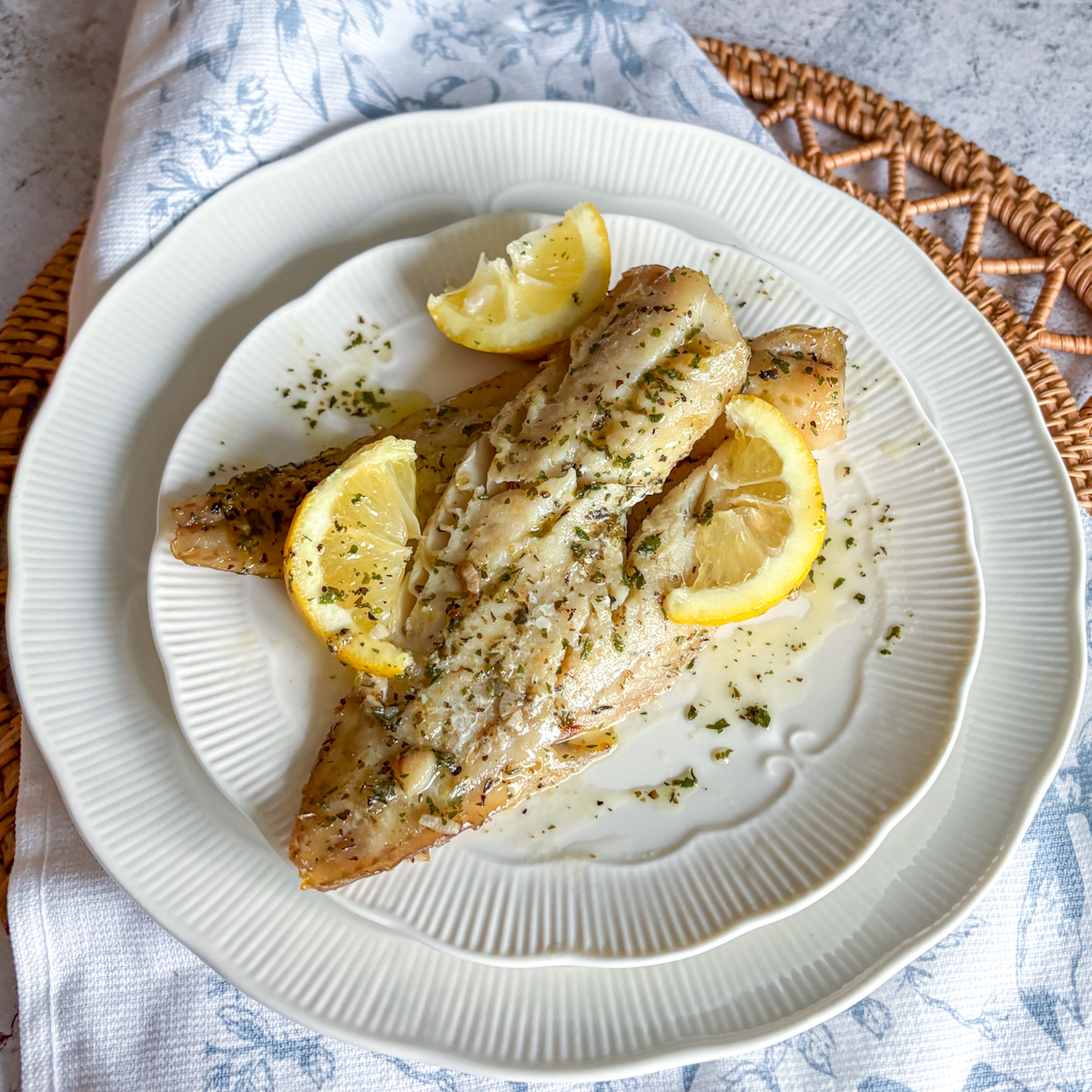 Baked pollock fillets with lemon slices and herbs on a white plate with butter sauce