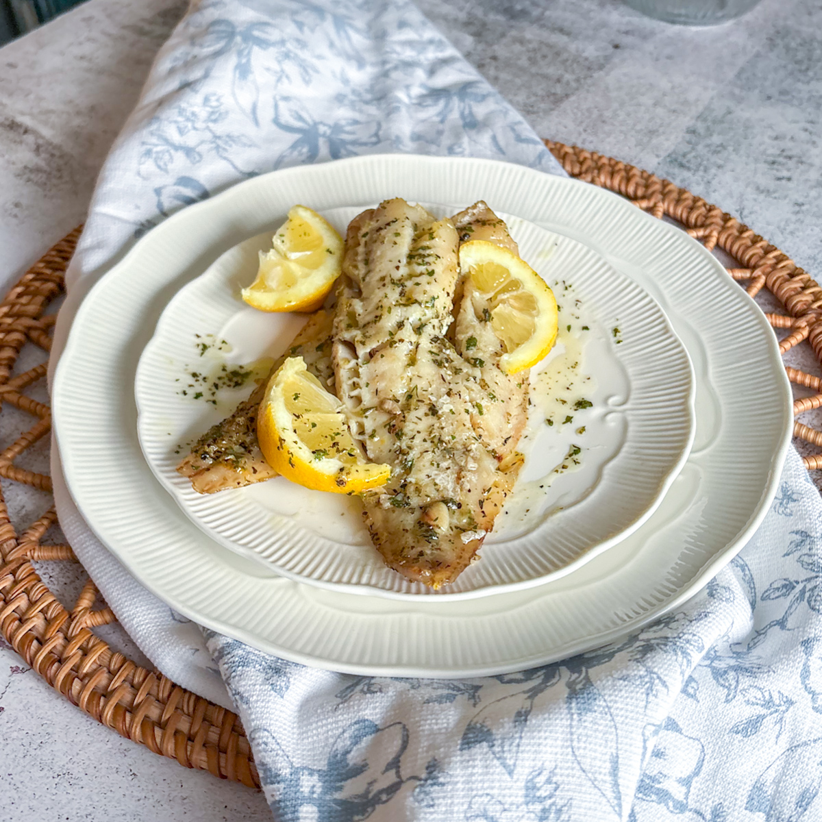 Baked pollock fillets plated with lemon slices and herb butter on a decorative white dish