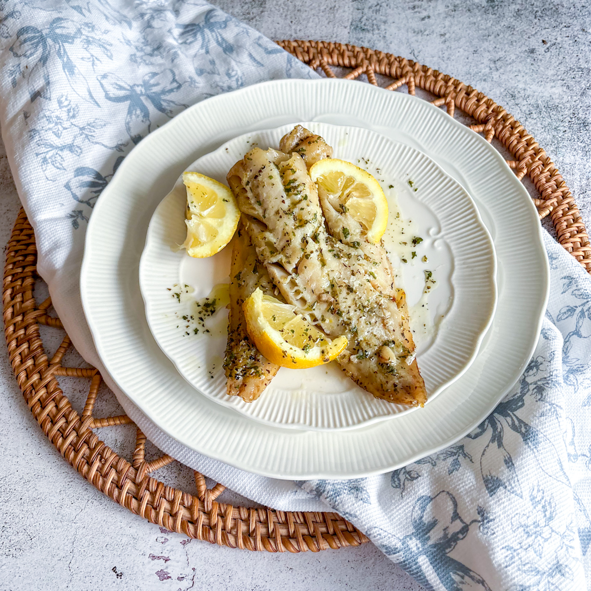 Baked pollock served with lemon wedges on a white plate, styled on a rustic table setting