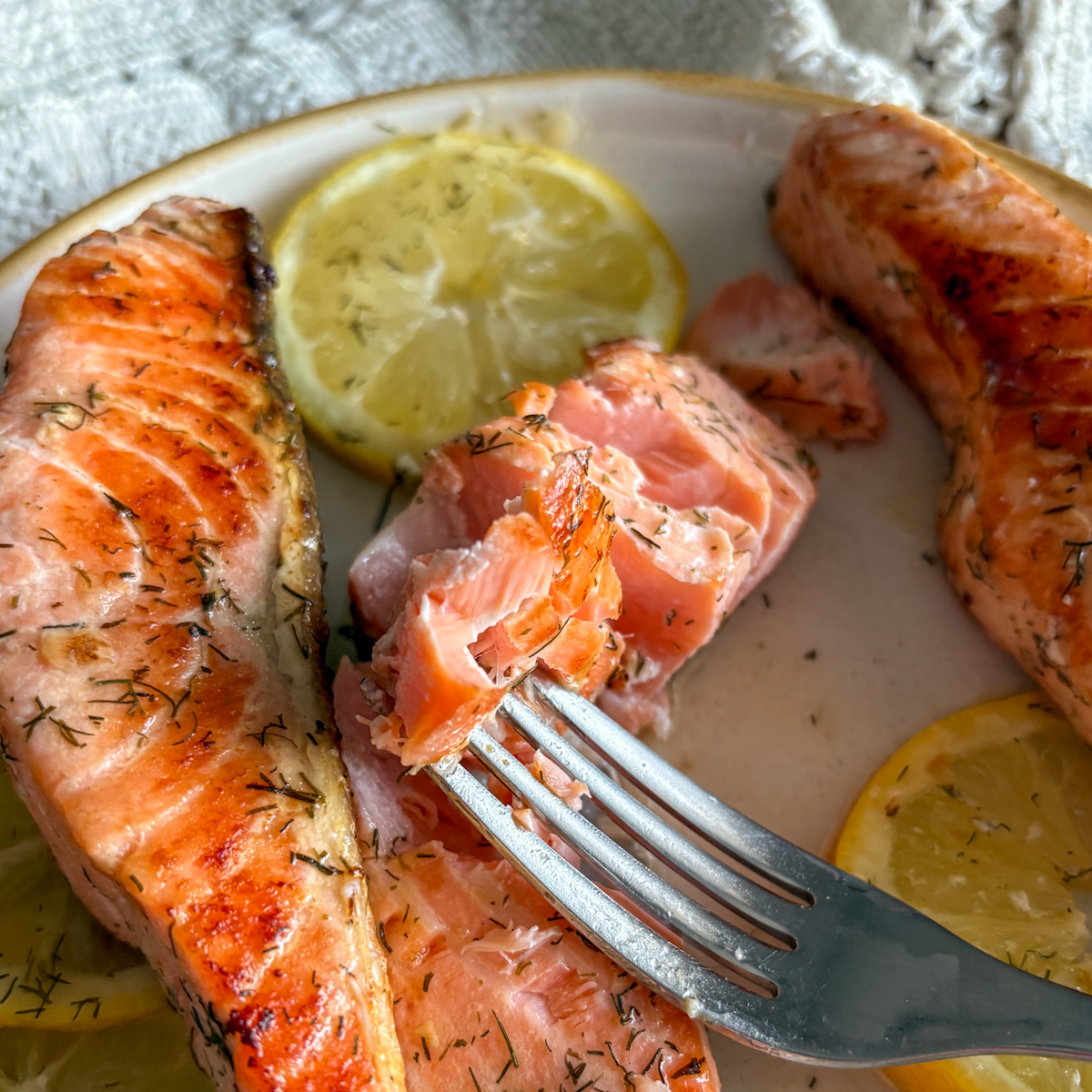 A close-up of a fork lifting a tender, flaky piece of pan fried salmon, showing the moist interior and the herb-rich butter coating.
