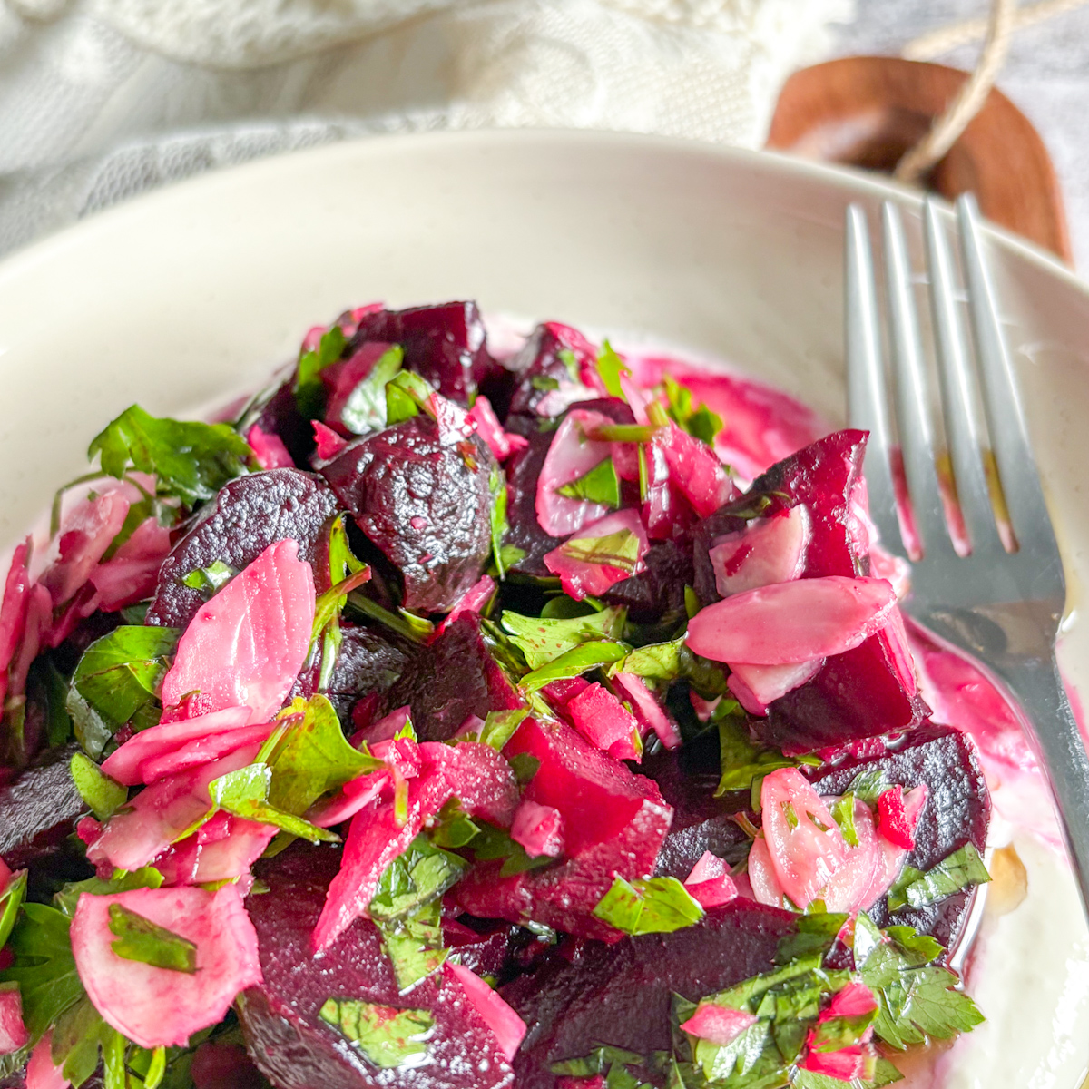 Roasted beet salad with sour cream dressing, fresh parsley, and shallots in a neutral ceramic plate