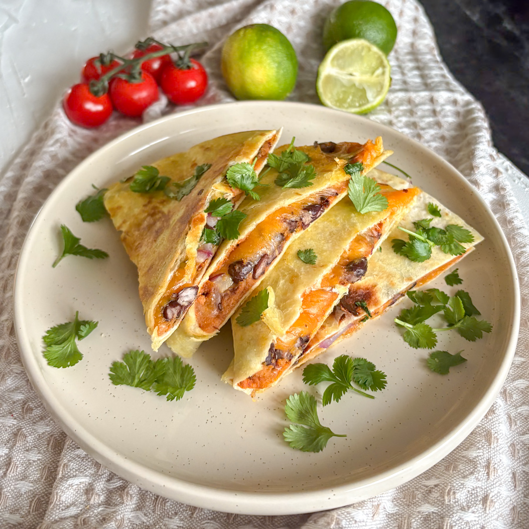 Crispy sweet potatoes quesadillas stacked on a round plate with fresh limes in the background, making a great meatless Monday recipe.