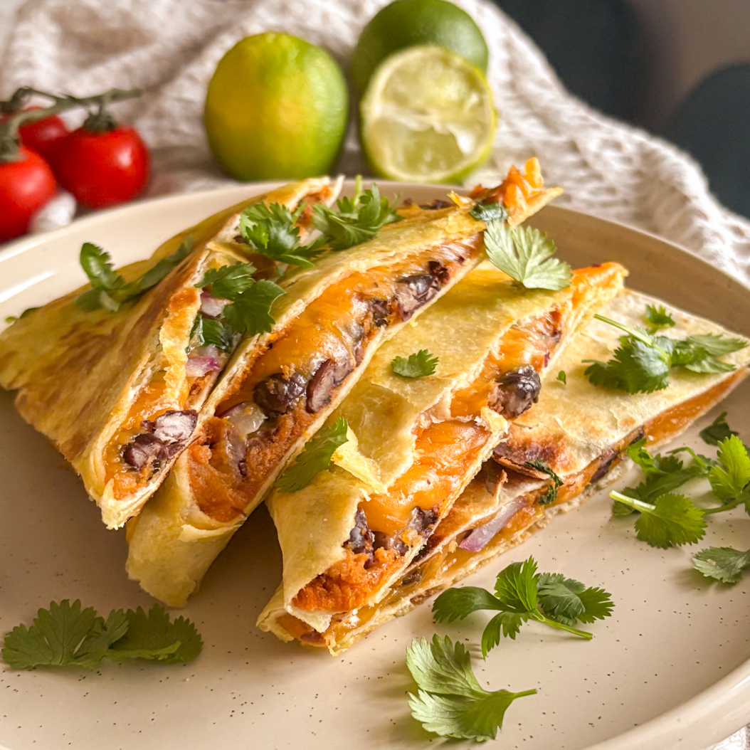 Close up of sliced sweet potatoes quesadillas on a speckled plate, showing the very filling and satisfying sweet potato and bean center.