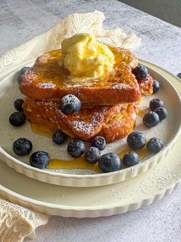 The best French toast recipe served as a thick stack, topped with melting vanilla ice cream, fresh blueberries, and a dusting of icing sugar.
