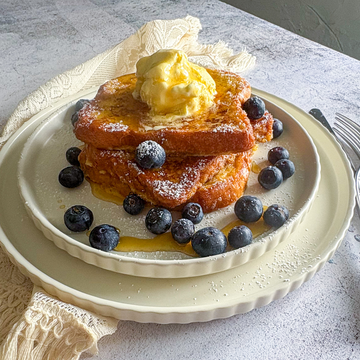 The best French toast recipe served as a thick stack, topped with melting vanilla ice cream, fresh blueberries, and a dusting of icing sugar.