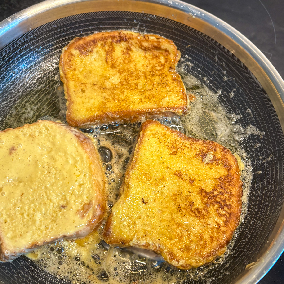 Frying soaked slices in unsalted butter using a heavy-based skillet until golden brown, demonstrating how to make French toast with thick bread.