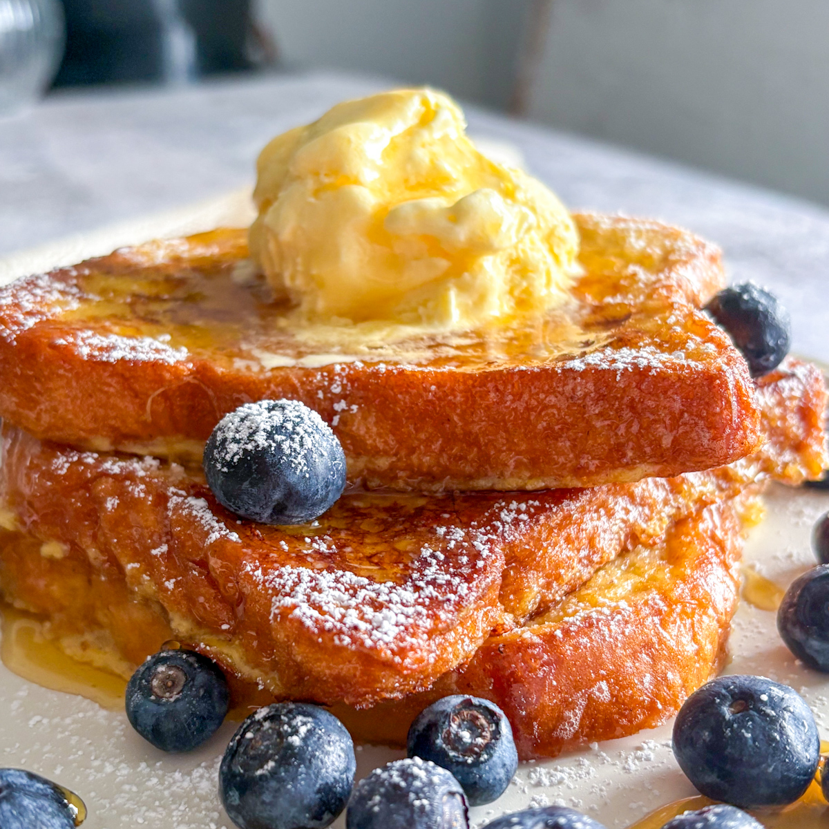 Close-up showing the rich egg custard crust of this easy homemade brioche French toast recipe, served warm with melting ice cream and powdered sugar.