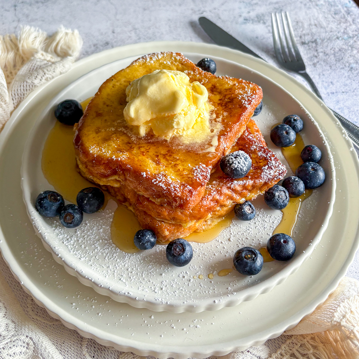 A beautiful plate of Brioche French Toast cooked to a crisp golden brown, topped with a scoop of ice cream and fresh blueberries.