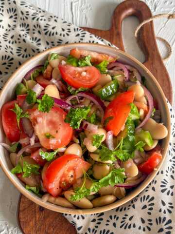 A vibrant bowl of healthy butter bean salad with red onion, cucumber, and meaty heirloom tomato wedges.
