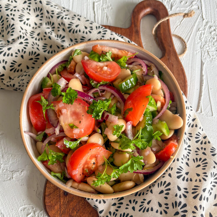 A vibrant bowl of healthy butter bean salad with red onion, cucumber, and meaty heirloom tomato wedges.