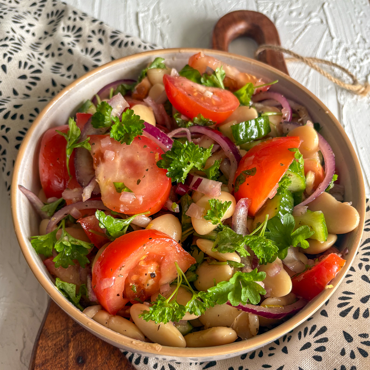 An easy butter bean salad with garlic dressing served in a ceramic bowl on a rustic wooden board.