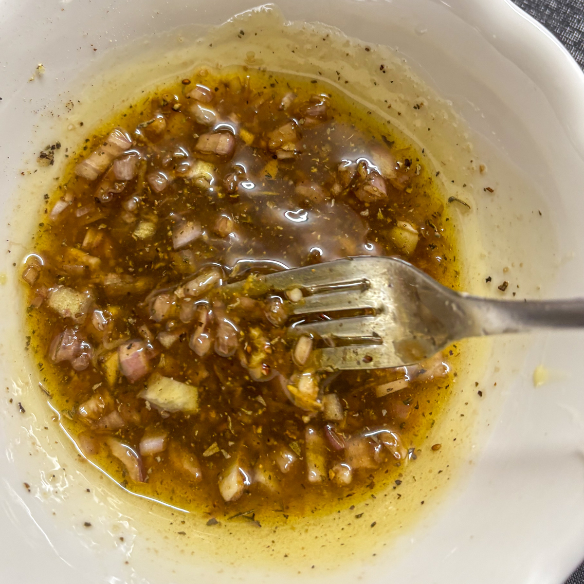 Whisking the garlicky dressing with a fork in a white bowl for a butter bean salad.