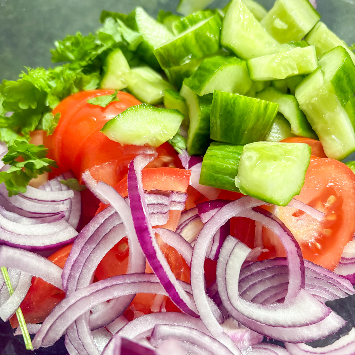 Chopped red onions, tomatoes, and deseeded cucumbers in a glass bowl for a butter bean salad recipe.
