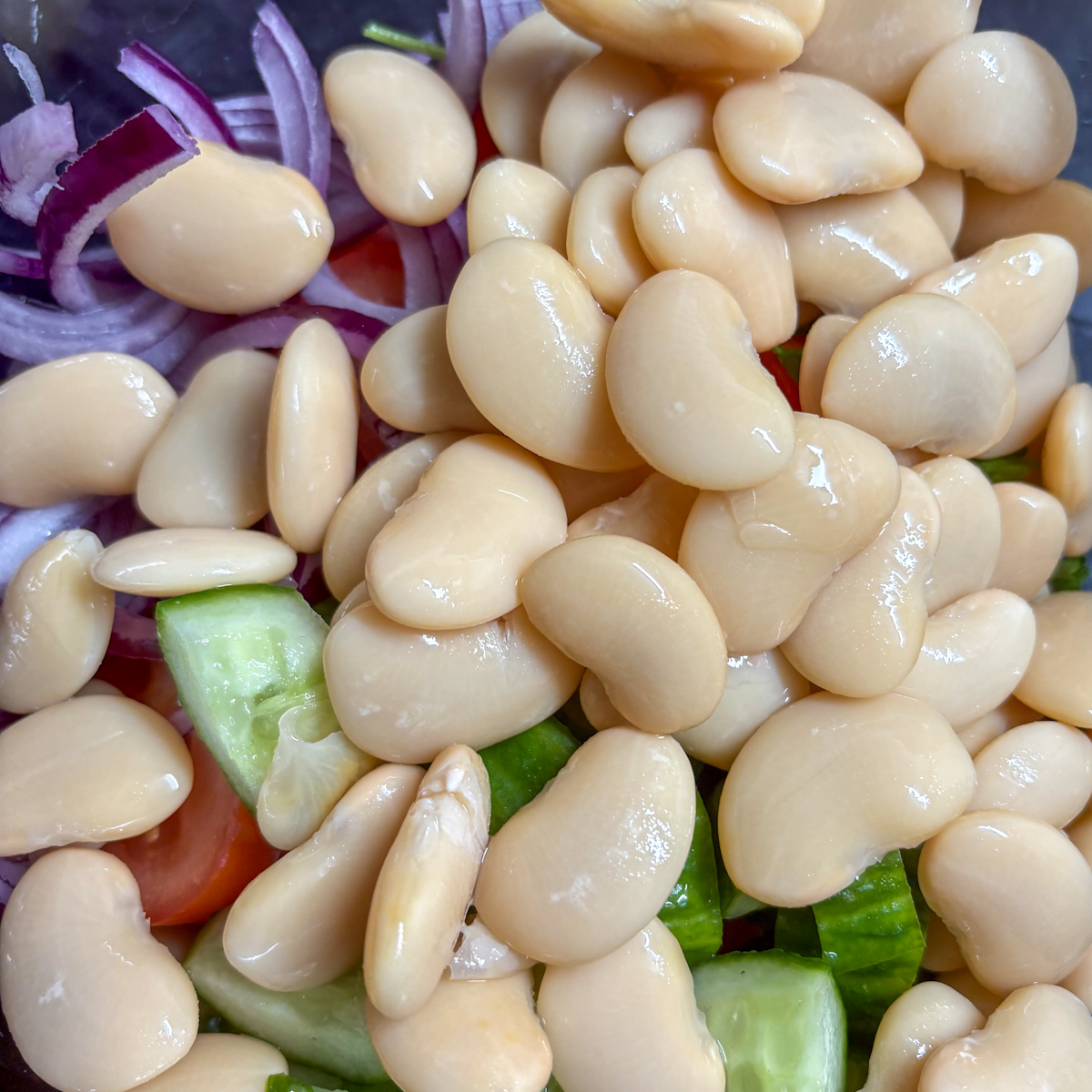 Rinsed tinned beans added to the bowl of chopped vegetables for a healthy butter bean salad.
