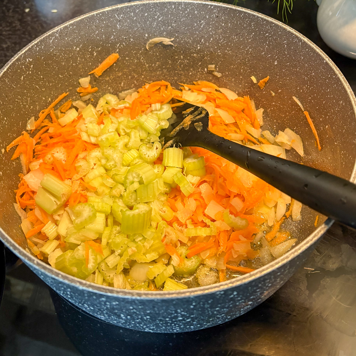 Grated carrots and chopped celery being sautéed in oil for a traditional Chicken Borscht recipe.