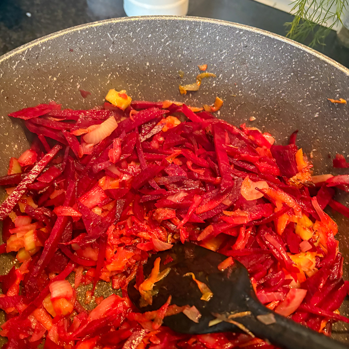 Sautéing julienned beets and onions in a pan to create the authentic base for Chicken Borscht.