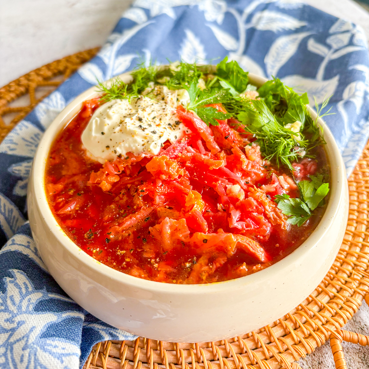 Hearty chicken borscht with shredded chicken, cabbage, and beetroot, topped with sour cream and herbs.