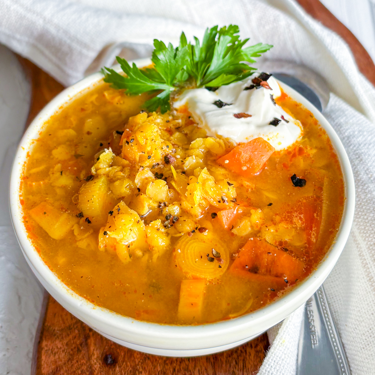 A white bowl filled with chunky lentil soup topped with sour cream and fresh herbs.