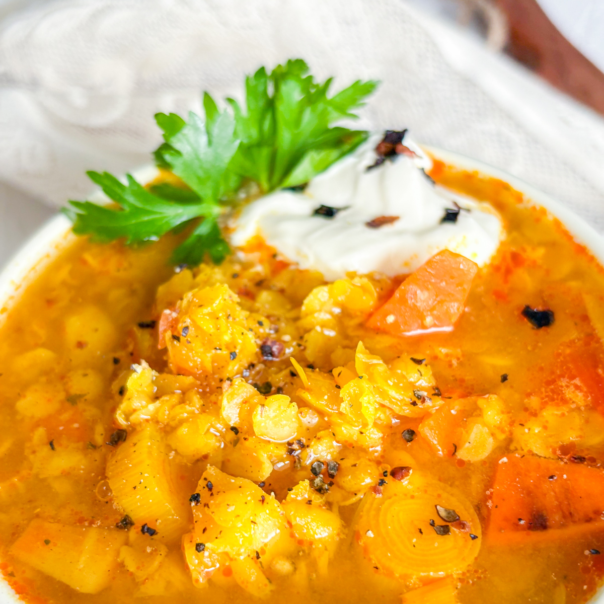 A close-up shot of a white bowl containing warming, chunky spiced red lentil soup garnished with coriander and sour cream