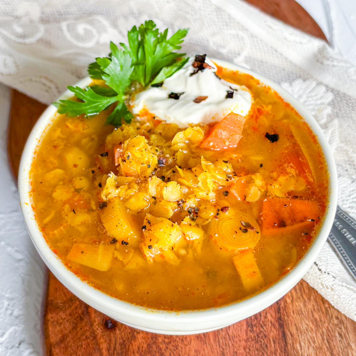 Final presentation of the vibrant orange healthy vegan spiced lentil soup in a white bowl, garnished with green herbs and red chili flakes.