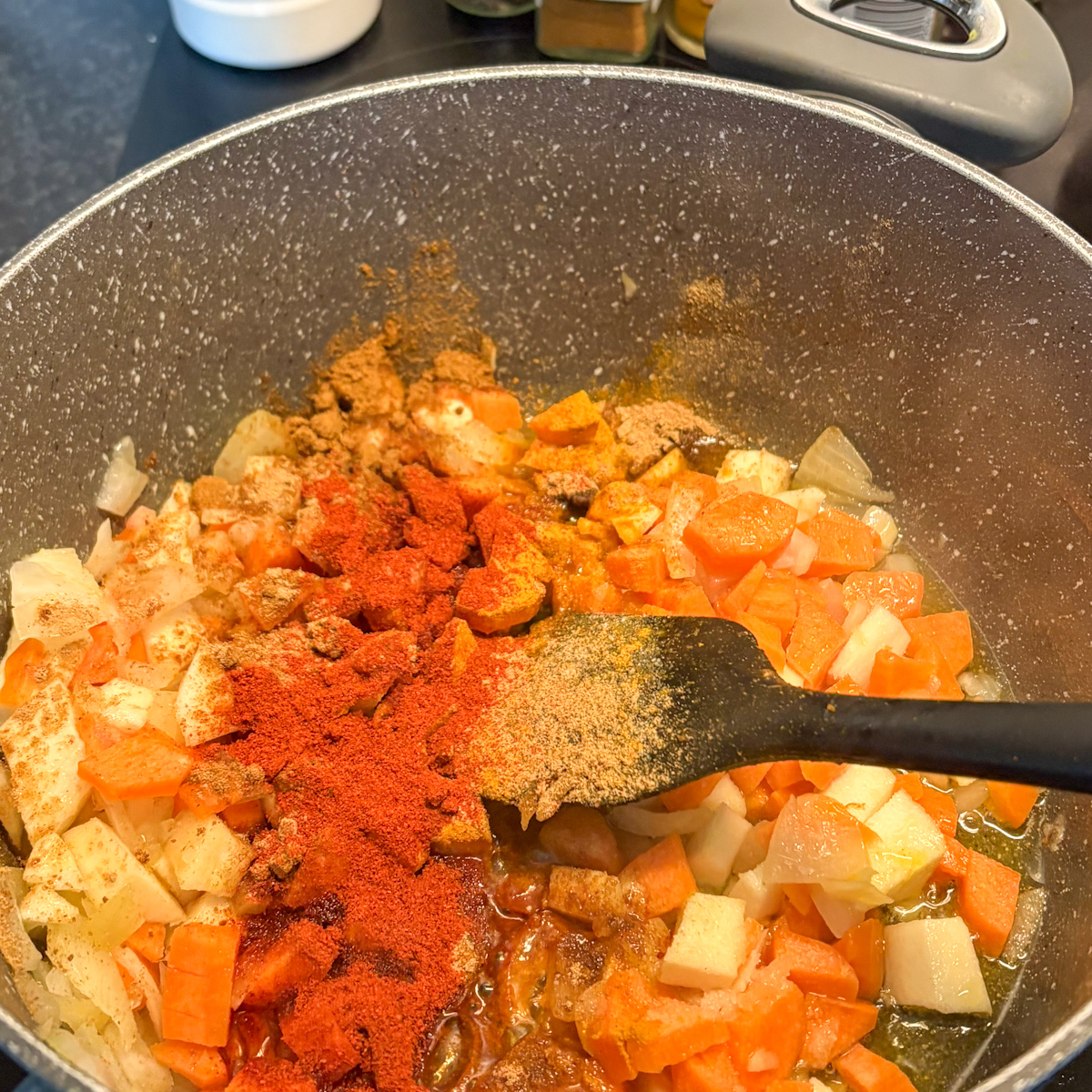 A close-up view of sautéed chopped carrots, parsnips, and onions in a large pot with ground spices, starting the base for a chunky lentil soup recipe.