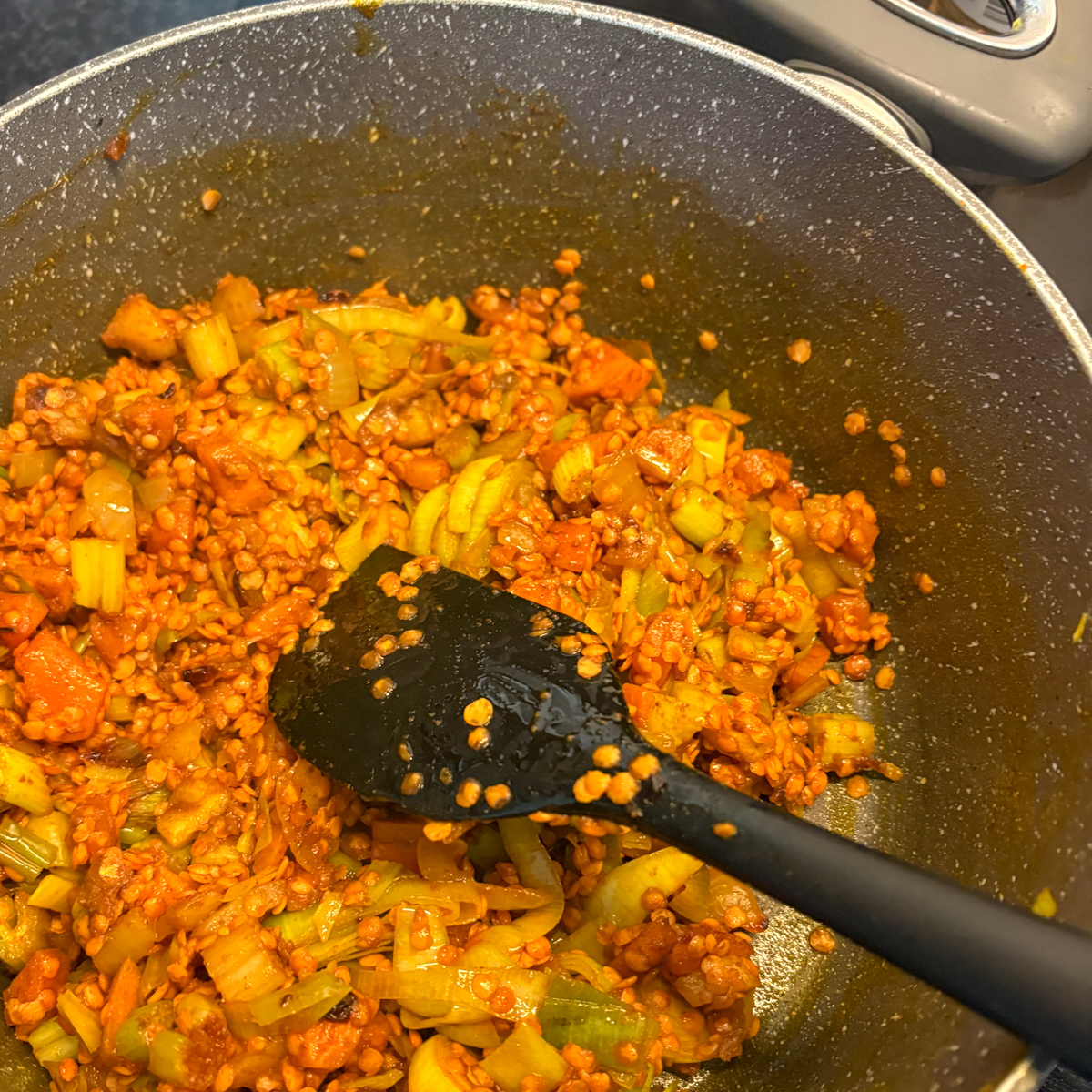 Washed red lentils being added from a mesh colander into the pot with the sautéed vegetables.